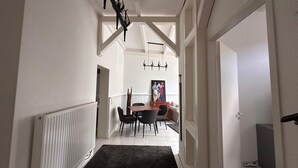 Een gang die uitkomt in een eetruimte met een tafel, stoelen, een radiator en een zwart vloerkleed.