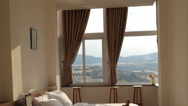 Habitación de hotel con dos camas, una ventana con cortinas, una mesita y un jarrón con flores.
