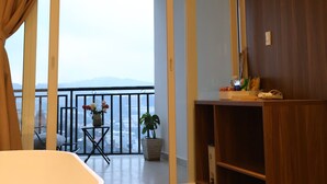 Una habitación con un ventanal grande, suelo de madera, una silla blanca y un armario de madera.
