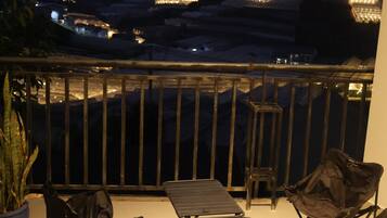 A balcony with a table and chairs, a potted plant, and a view of distant lights and mountains.