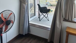 Una habitación con ventana, ventilador y una silla.