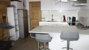 Een moderne keuken met een centraal eiland, barkrukken, een koelkast en een houten deur.
