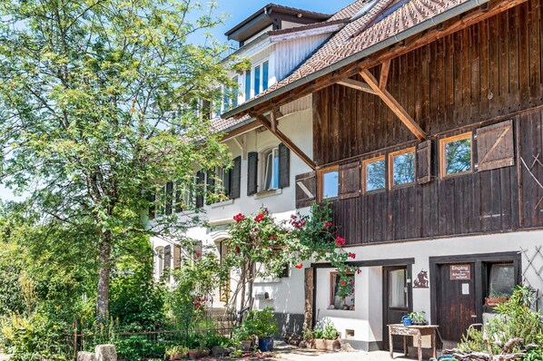 A traditional wooden building with a balcony, a garden with potted plants, and a sign indicating a restaurant.