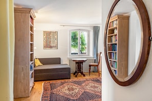 Una habitación con un sofá, una estantería de madera, un espejo redondo y una ventana con vista a la vegetación.