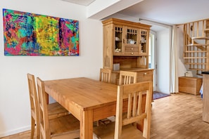 Una mesa de comedor de madera con sillas, un aparador con puertas de cristal y un cuadro abstracto y colorido en la pared.