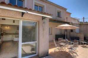 A house with a patio area featuring a table and chairs, a sliding glass door leading to a kitchen, and a balcony with a railing. - Charming 1-Bedroom Apartment Near Beaches and Amenities (Eccica-Suarella)