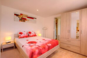 A bedroom with a bed, bedside tables, a wardrobe, and a painting on the wall. - Charming 1-Bedroom Apartment Near Beaches and Amenities (Eccica-Suarella)