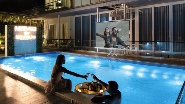 A swimming pool with a bar area, a large illuminated sign, and a view of the pool from inside a building. - Alaya Stays Parinita Farm 4 BHK Villa (Faridabad)