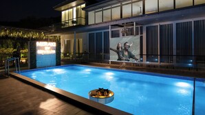 A swimming pool with a lounge area, a modern building with large windows, and a sign that reads 'MERAKI'. - Alaya Stays Parinita Farm 4 BHK Villa (Faridabad)
