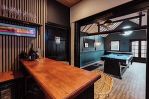 Zona de bar con mesa de billar, un cartel que indica 'Se sirve ginebra' y un letrero de 'Baños'.