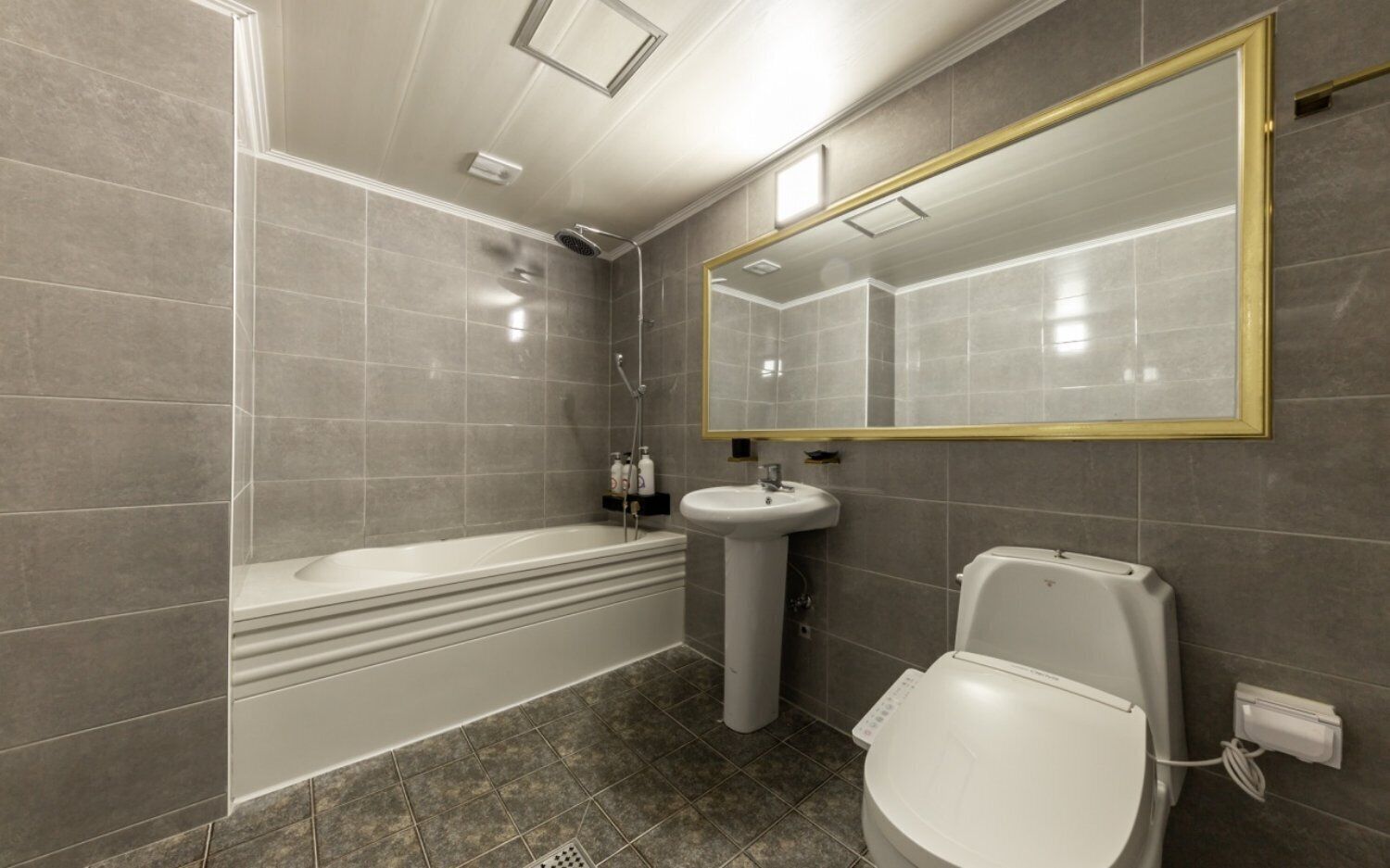 Een badkamer met een bad, een wastafel op voet, een toilet en een grote spiegel met gouden lijst.