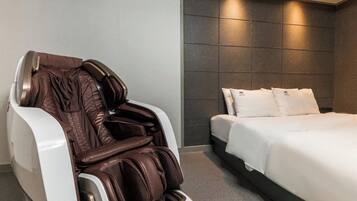 Una habitación de hotel moderna con una silla de masajes, una cama bien hecha y una pared de baldosas oscuras.
