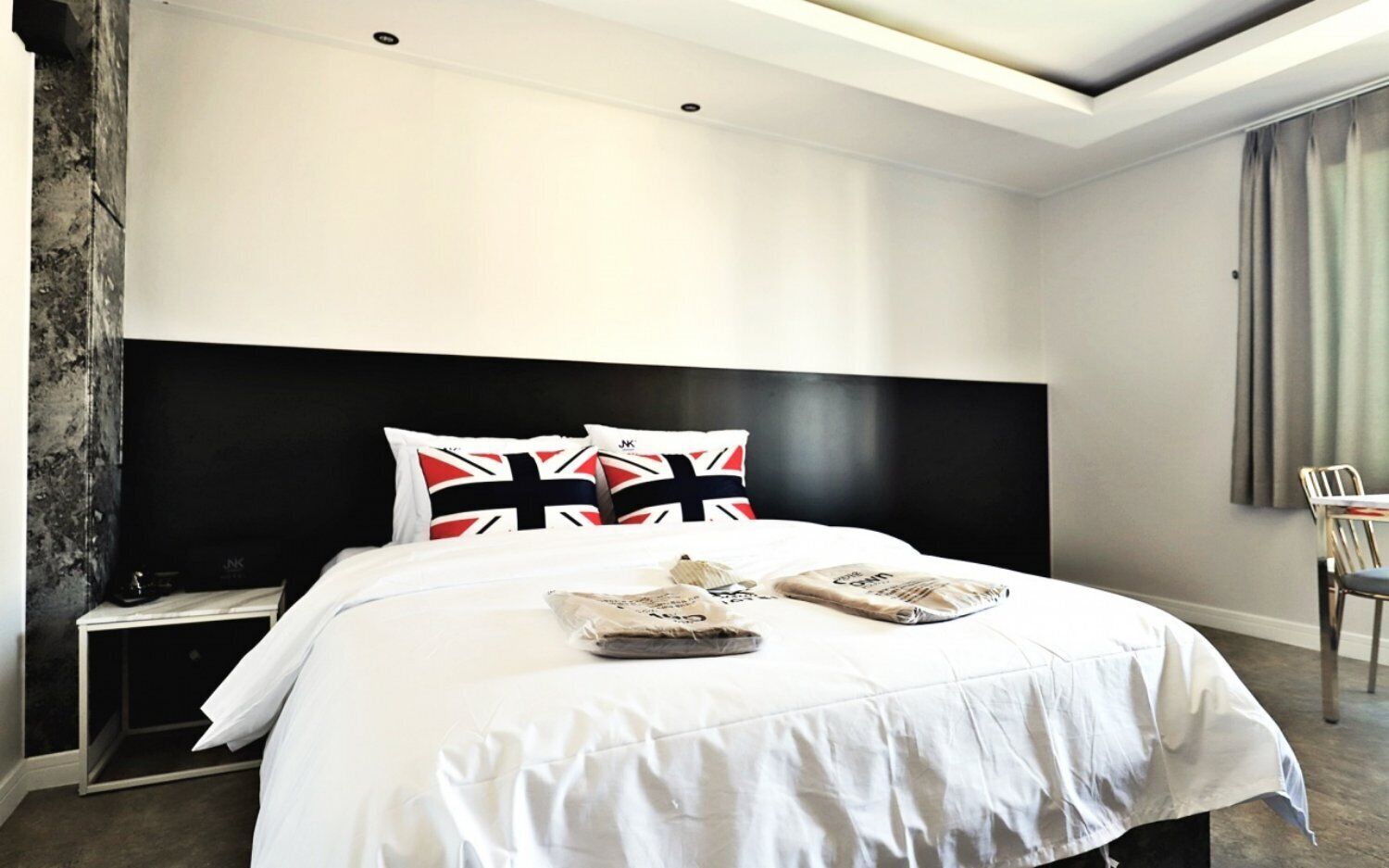 Quarto de hotel moderno com uma cama grande, cabeceira preta e mesa de cabeceira com abajur.