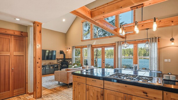 A kitchen with wooden cabinets, a large island, and a stone fireplace. - Lakebay Hideaway: Private Lakefront House on the Key Peninsula (Home)