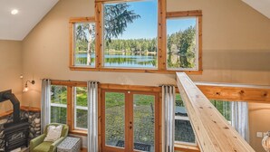 A room with a stone fireplace, a green armchair, and a view of a lake through large windows. - Lakebay Hideaway: Private Lakefront House on the Key Peninsula (Home)