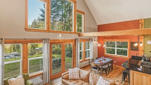 A spacious loft-style room with a dining area, a kitchen, and large windows offering views of the outdoors. - Lakebay Hideaway: Private Lakefront House on the Key Peninsula (Home)