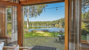 A room with a large sliding glass door leading to a patio with a view of a lake and forest. - Lakebay Hideaway: Private Lakefront House on the Key Peninsula (Home)