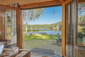 Una habitación con un amplio ventanal corredero que da a un patio con vistas a un lago y un bosque.