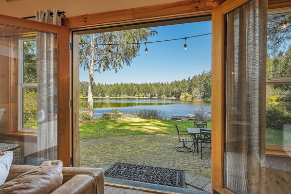 Una habitación con un amplio ventanal corredero que da a un patio con vistas a un lago y un bosque.