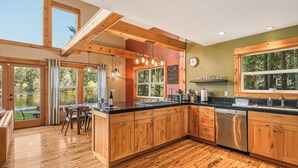 A modern kitchen with wooden cabinets, a dishwasher, and a dining area with a table and chairs. - Lakebay Hideaway: Private Lakefront House on the Key Peninsula (Home)