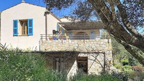 Una casa de piedra de dos pisos con un balcón, rodeada de vegetación.
