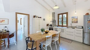 Una cocina con una mesa de madera, sillas blancas, un refrigerador y una ventana con vistas.