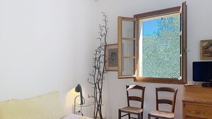 Un dormitorio con cama, dos sillas, cómoda, escritorio, lámpara y ventana con vistas.