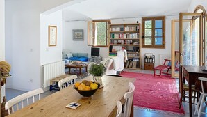 Una sala de estar acogedora con una mesa de comedor de madera, una estantería, un televisor y una alfombra roja.