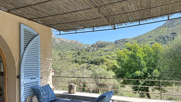 Un balcón con un sofá de mimbre, techo de paja y vista a un paisaje montañoso.