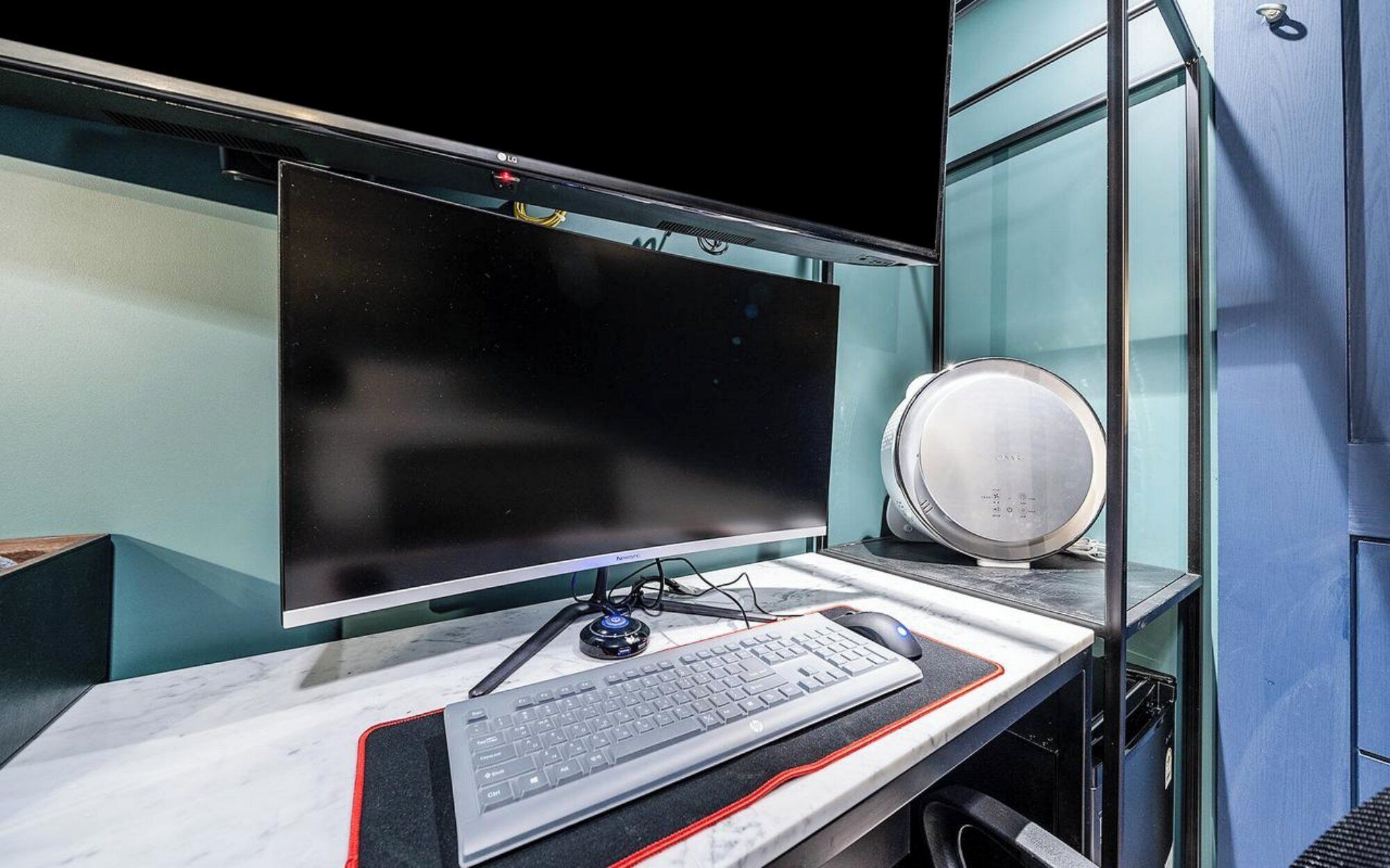 A modern office desk with a flat-screen monitor, keyboard, mouse, and a round speaker.