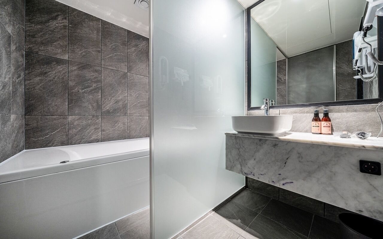 A modern bathroom with a glass-enclosed shower, a white sink, and a marble countertop.