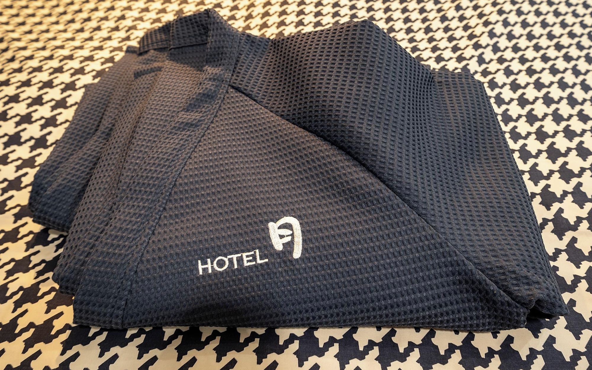 A folded dark blue hotel garment with a logo on it, placed on a patterned floor.