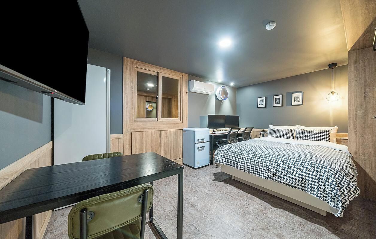 A compact room with a bed, a desk, a chair, a small fridge, and a TV.
