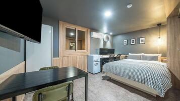 A compact room with a bed, a desk, a chair, a small fridge, and a TV.