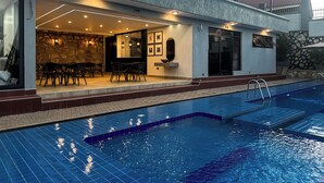 A modern outdoor pool area with a stone wall, a dining area with chairs, and a poolside bar. - Vee Hotel Apartments (Entebbe)