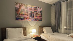 A hotel room with two beds, a nightstand with a lamp, a painting of a building, and a window with curtains. - Vee Hotel Apartments (Entebbe)