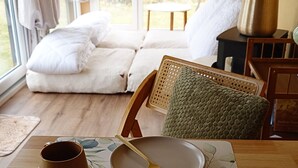 Una habitación acogedora con sofá, sillón, una mesa con taza y plato, y ventana con cortinas.