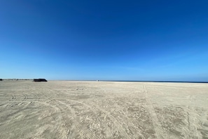 A vast, open sandy area with tire tracks and a distant structure.