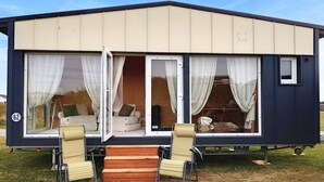 Una casa móvil con un dormitorio, un baño y un pequeño porche con dos sillas.