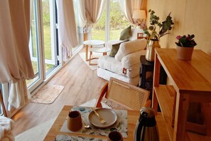 A cozy room with a sofa, a dining table with a placemat, a coffee pot, and a view of the outdoors through large windows.