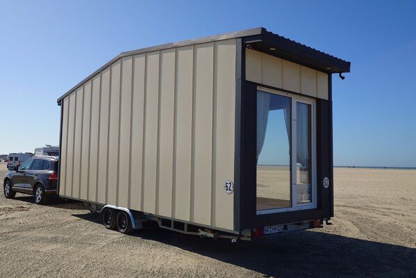 A beige trailer with a sliding door, a license plate, and a small awning.