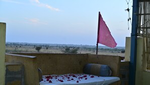 Un letto singolo con lenzuolo e cuscini bianchi, una bandiera rosa e vista su un paesaggio desertico.