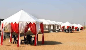 Une rangée de tentes blanches, ornées de rideaux rouges, sur une plage de sable.