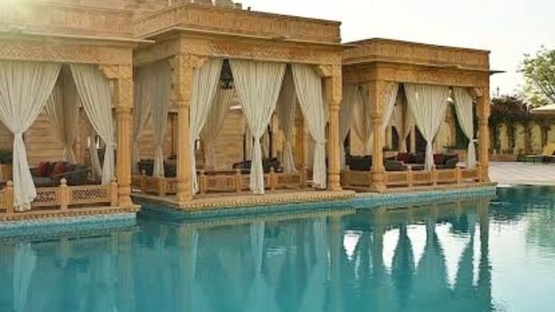 Una piscina con il suo riflesso, un edificio con un balcone e un cielo sereno.