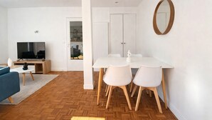 Een moderne woonkamer met een televisie, bank en een eethoek met stoelen en een tafel.