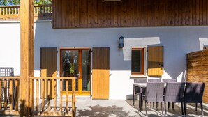 Eine Holzterrasse mit Gartenmöbeln, einer Schiebetür und einem Fenster mit Rollläden.