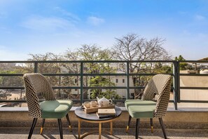 A balcony with two chairs, a table, and a tray with a teapot, cups, and books. - Alaya Stays Liv Regalia Apartments (Gurugram)