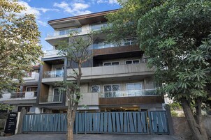 A multi-story residential building with balconies, a gated entrance, and surrounding trees.