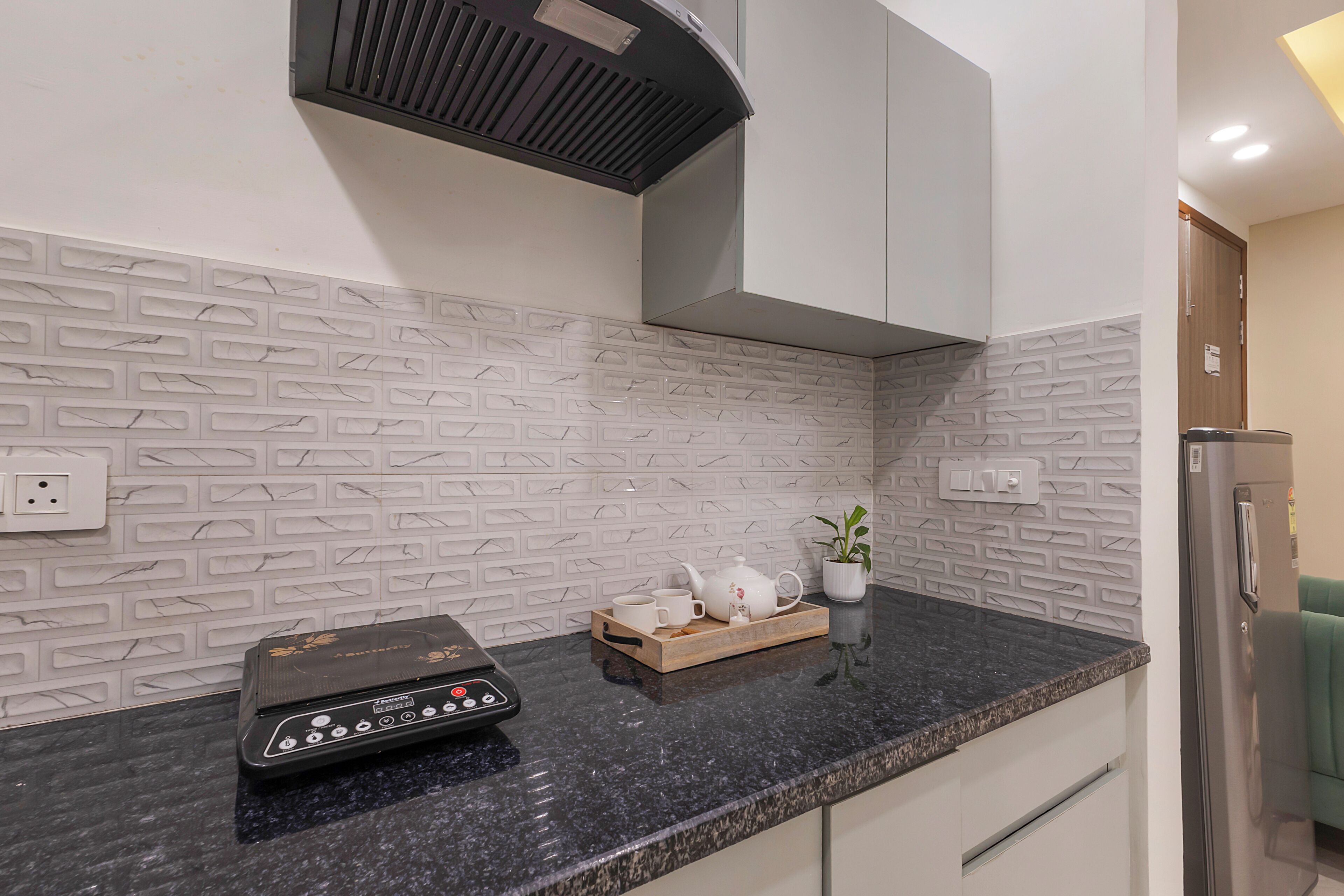 A kitchen with a black countertop, white tiled backsplash, a coffee maker, and a potted plant.