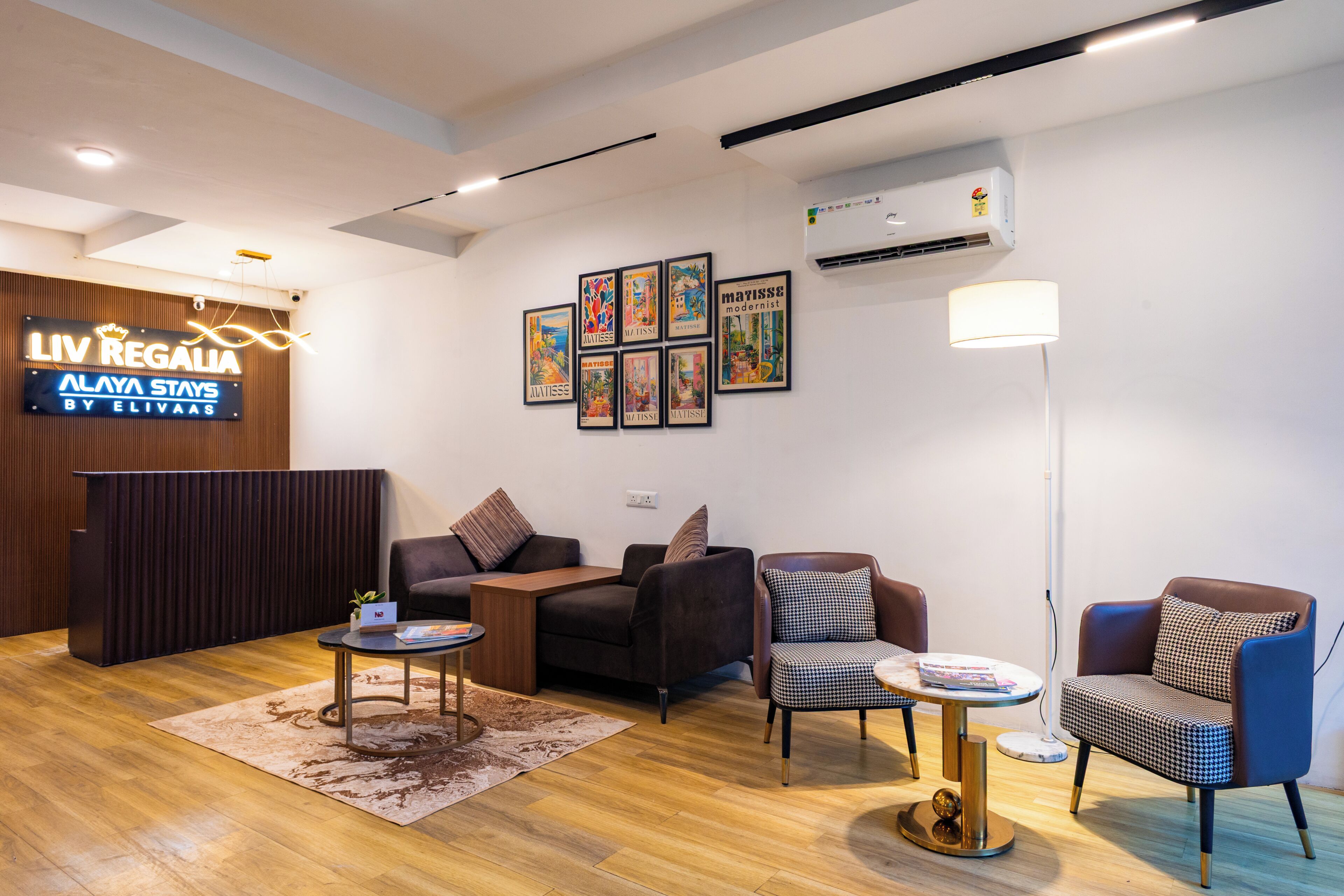 Un área de recepción moderna con un mostrador de madera, un sofá negro, un sillón estampado, una mesa redonda y una lámpara de pie.